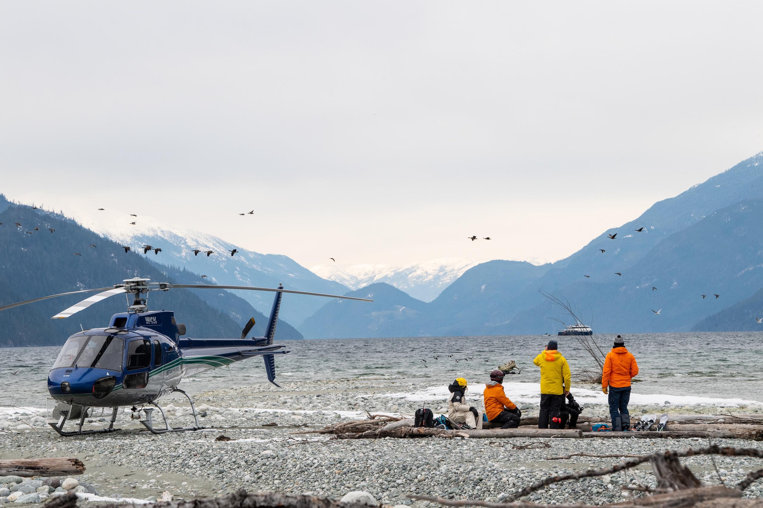 A group of skiers on the beach next to a helicopter