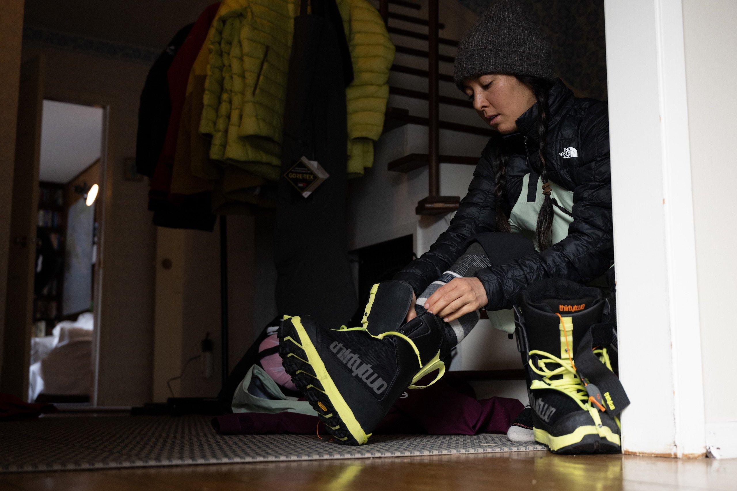 A woman putting on snowboard boots