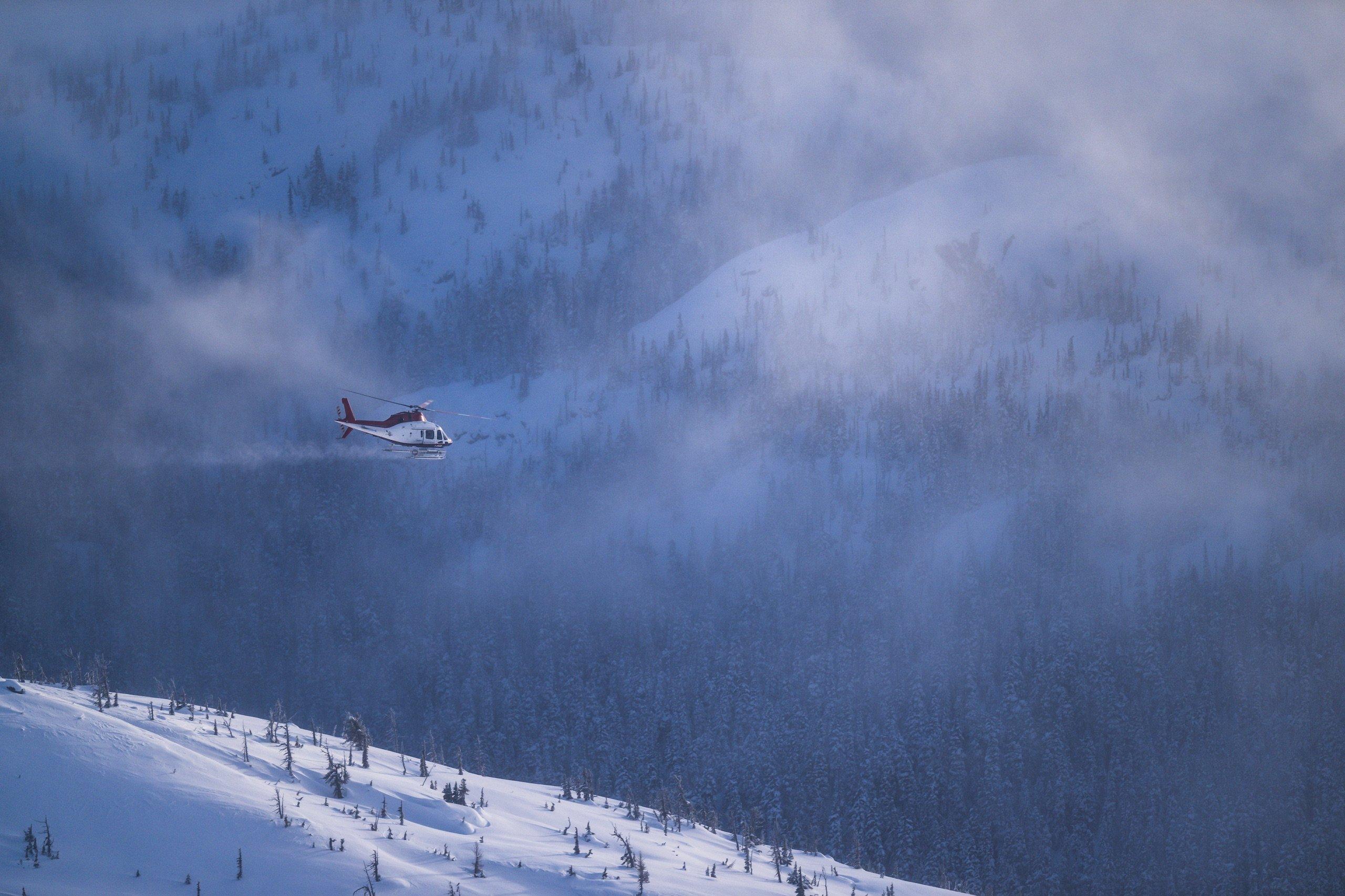 A red and white helicopter flying away from a mountain