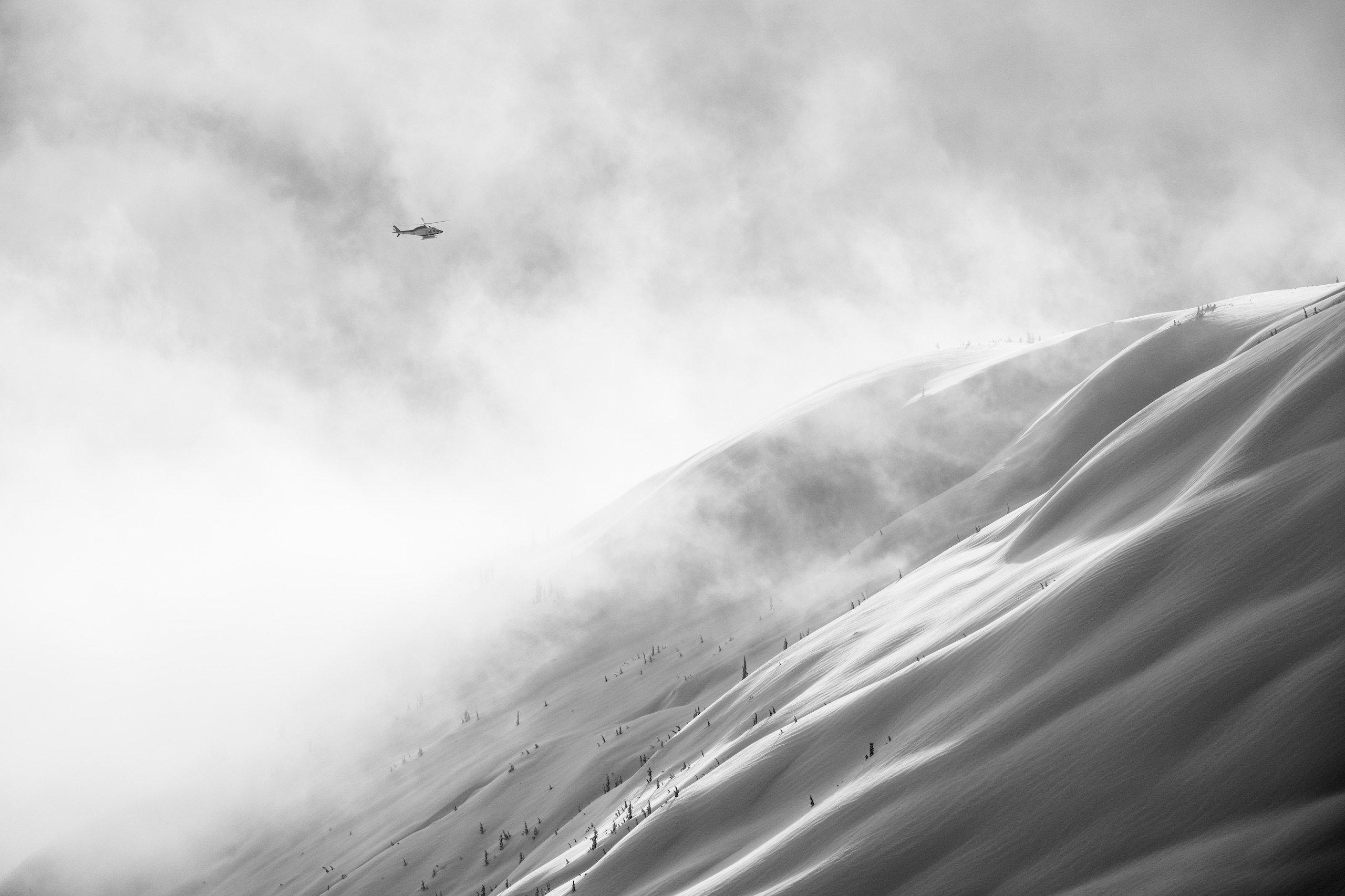 A helicopter flying over the mountain in a snowy mist