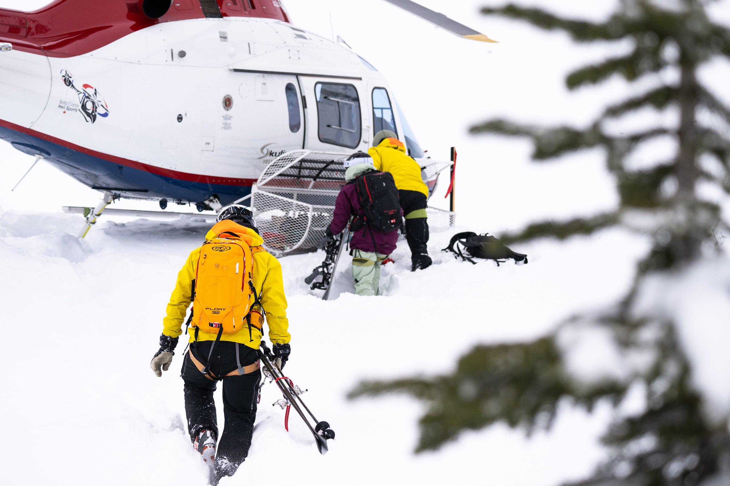 two ski guides and a heli skier approaching a helicopter