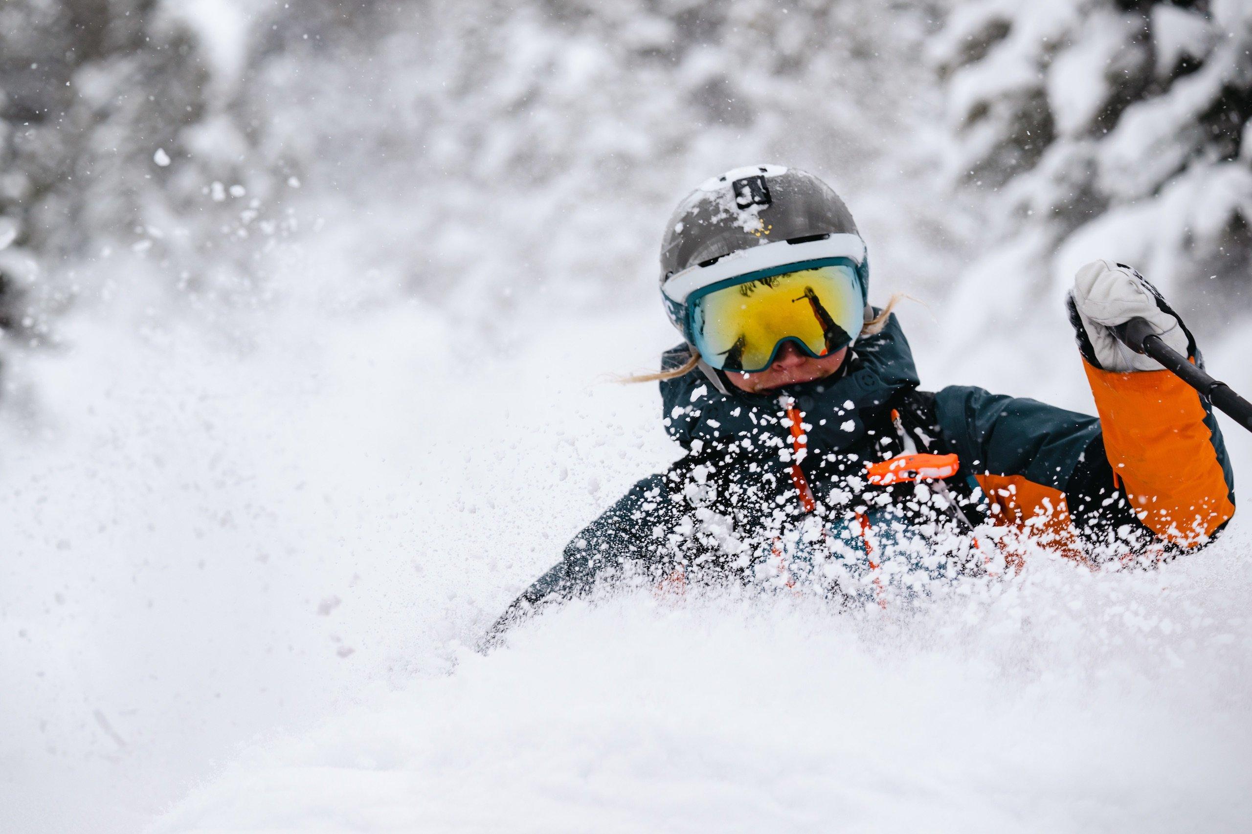 A skier in an orange jacket with a plume of snow in front of them