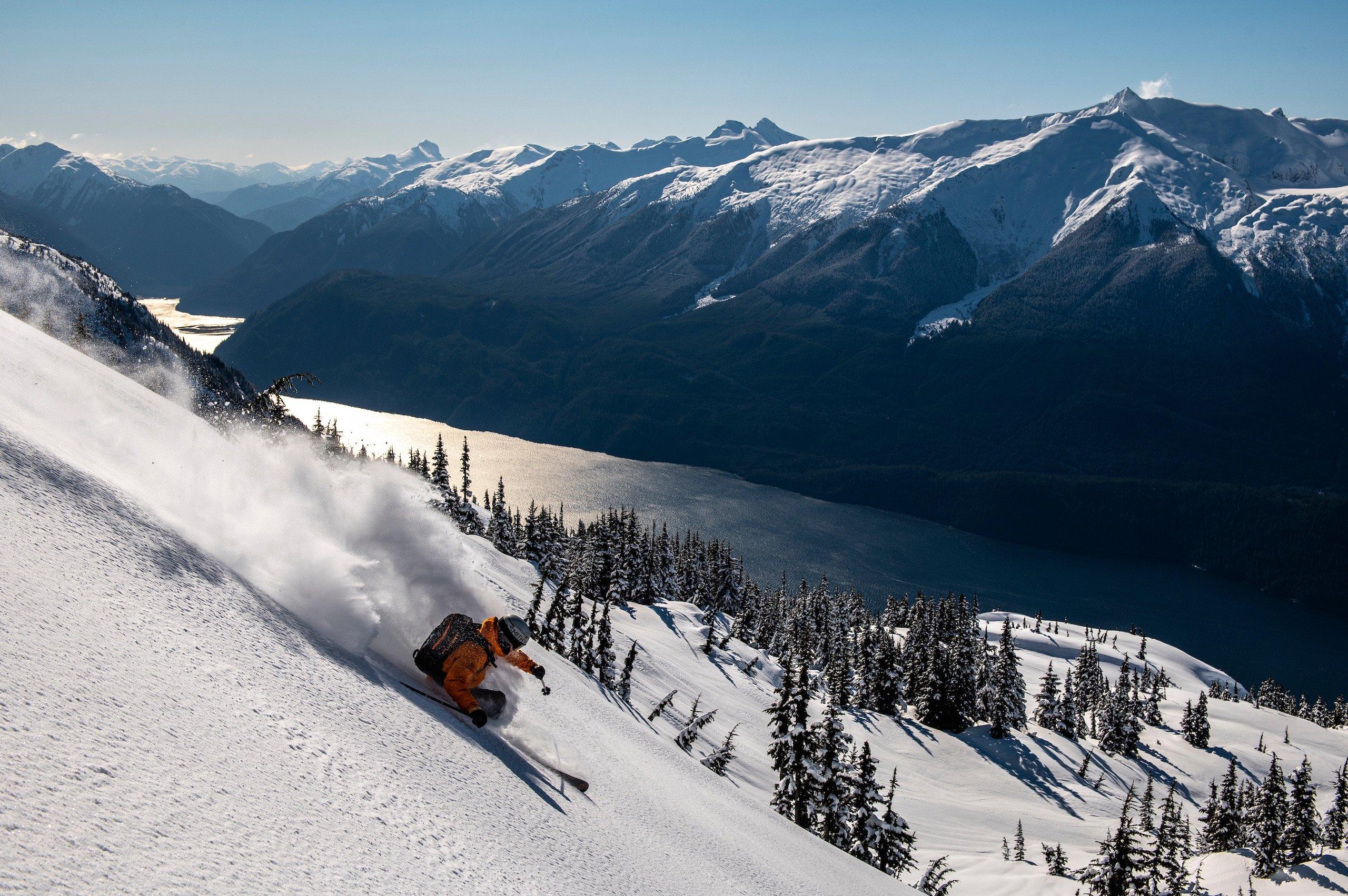 A skier in a orange jacket descending a mountain