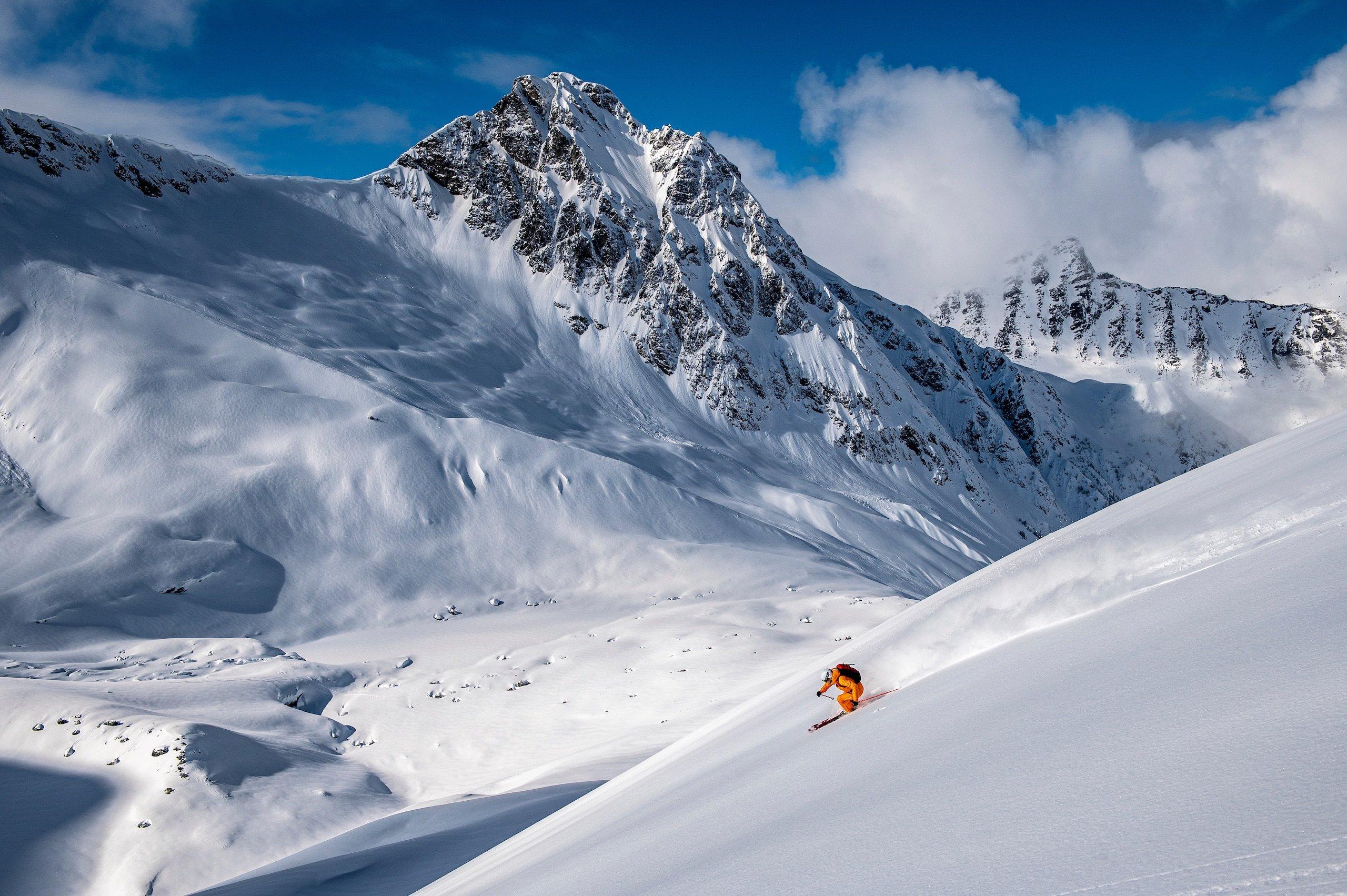 A person in a orange snowsuit skiing down a mountain