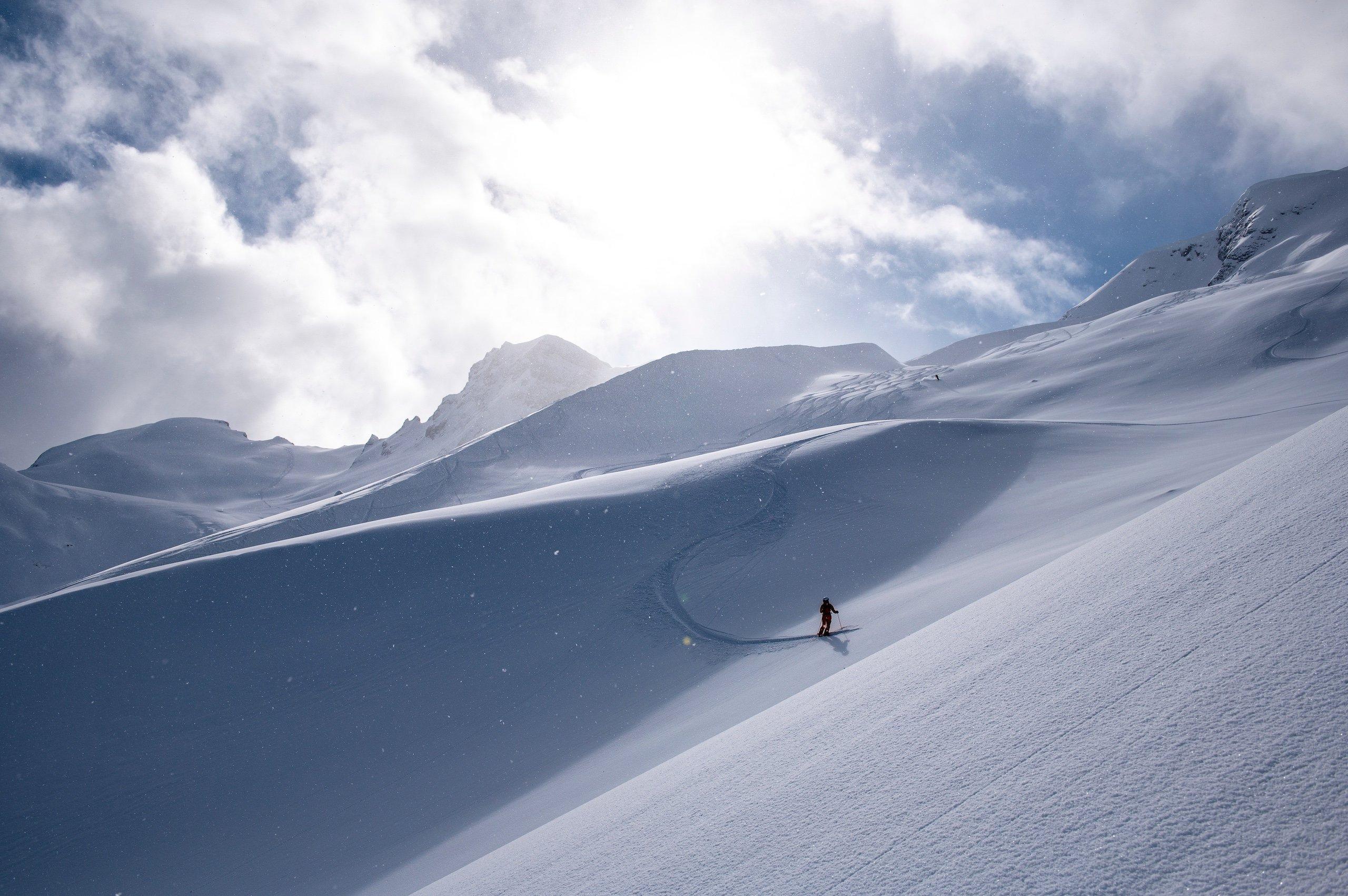 A skier on a mountain with clouds in the sky