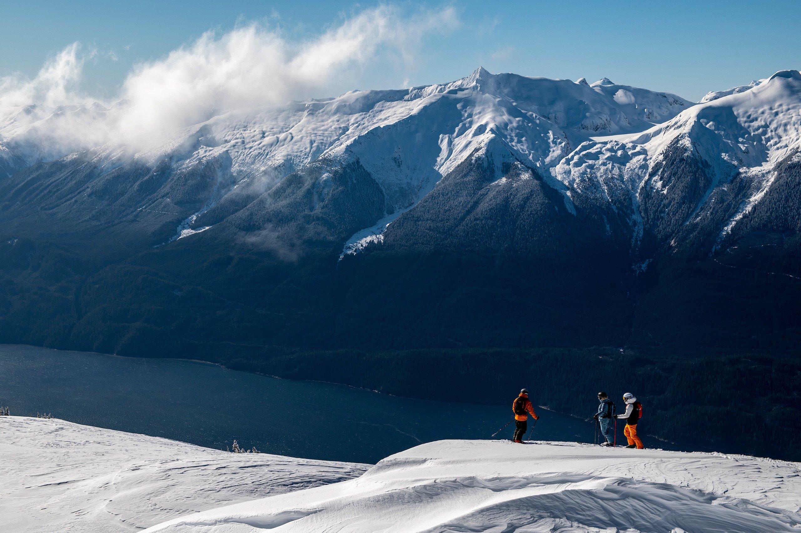 a group of skiers resting on flat ground looking at the water below them