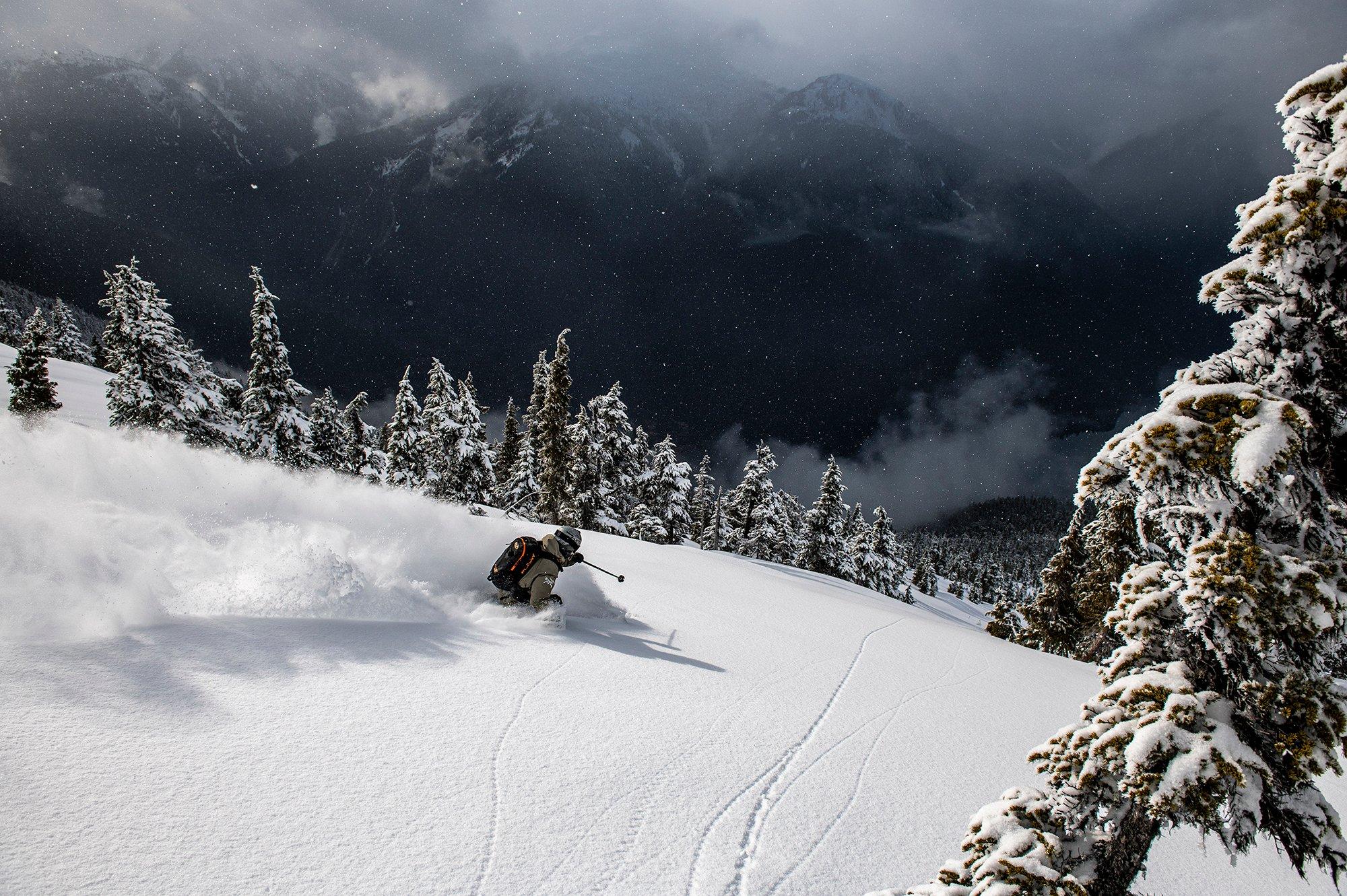 a man in a grey jacket skiing through the trees in waist deep powder