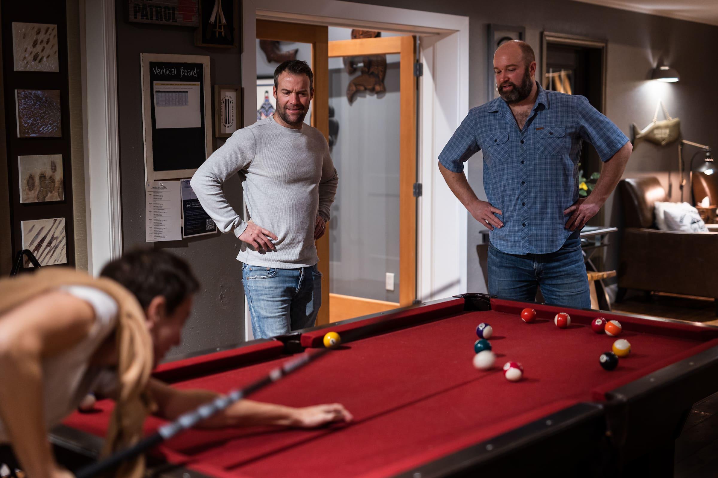 three men playing pool on a red pool table