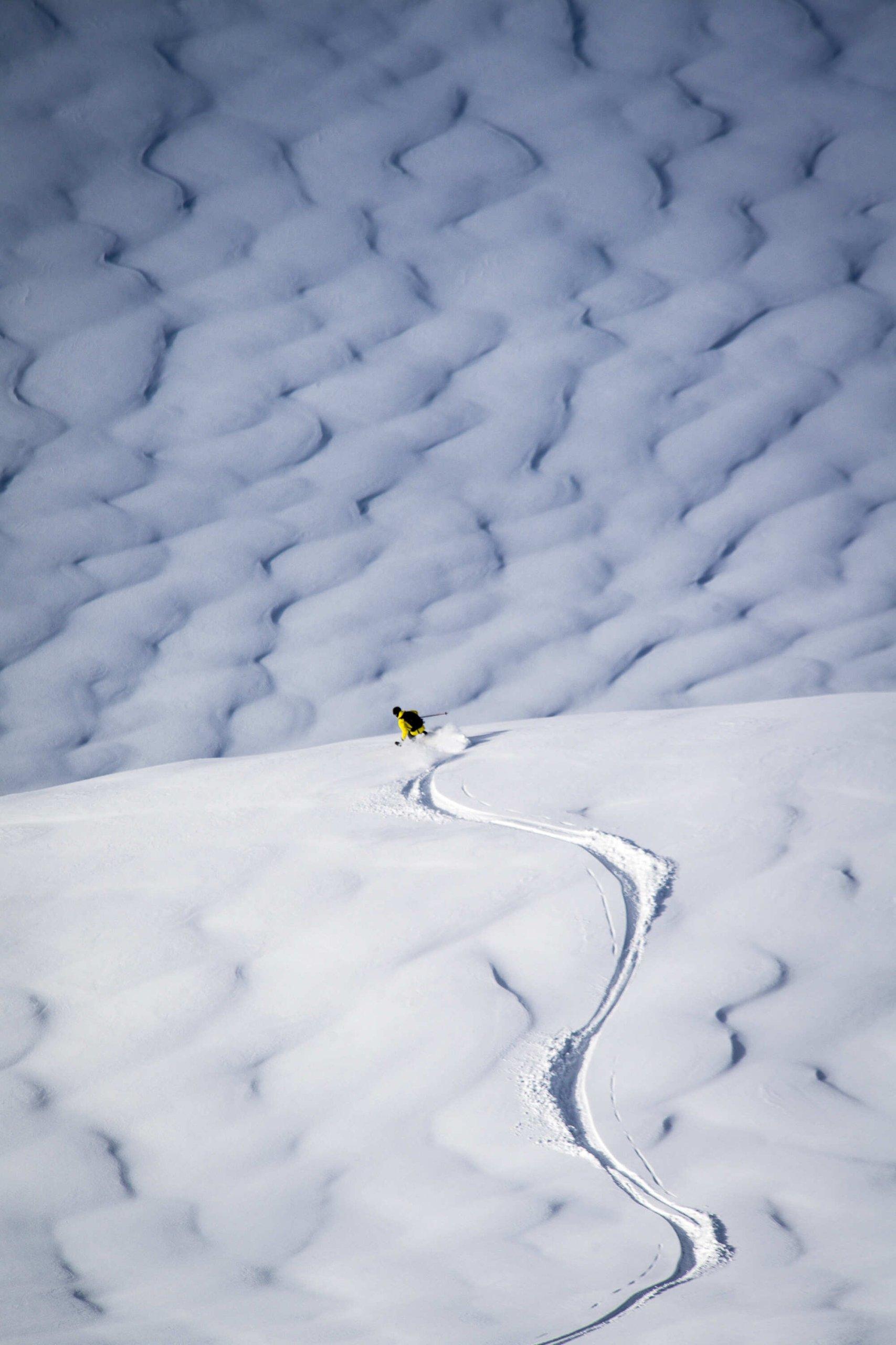 A skier in a yellow snowsuit descending a snowy mountain