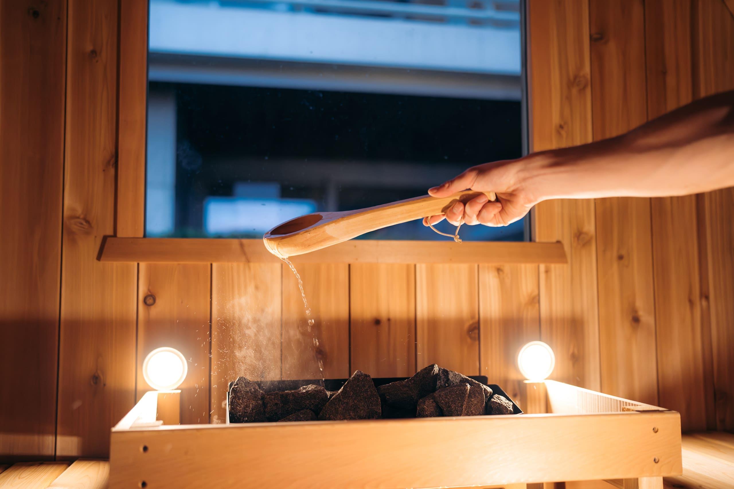 a wooden spoon being used to put water on the hot rocks of a wood sauna