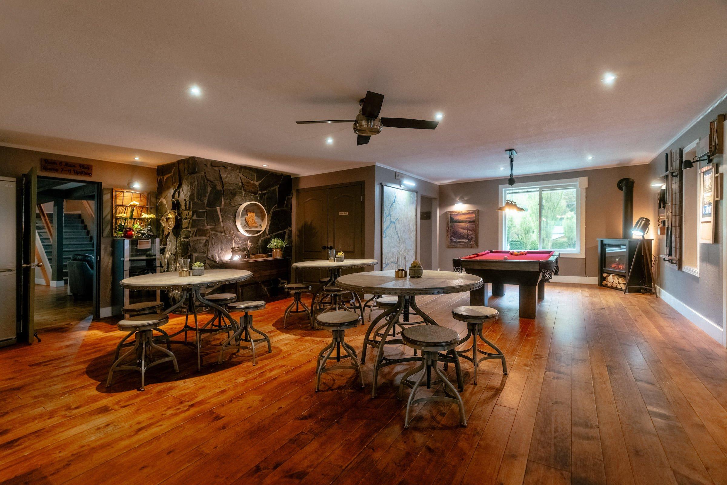 The inside of a wilderness lodge containing hard wood floors, a lounge with three tables, and a billiards table
